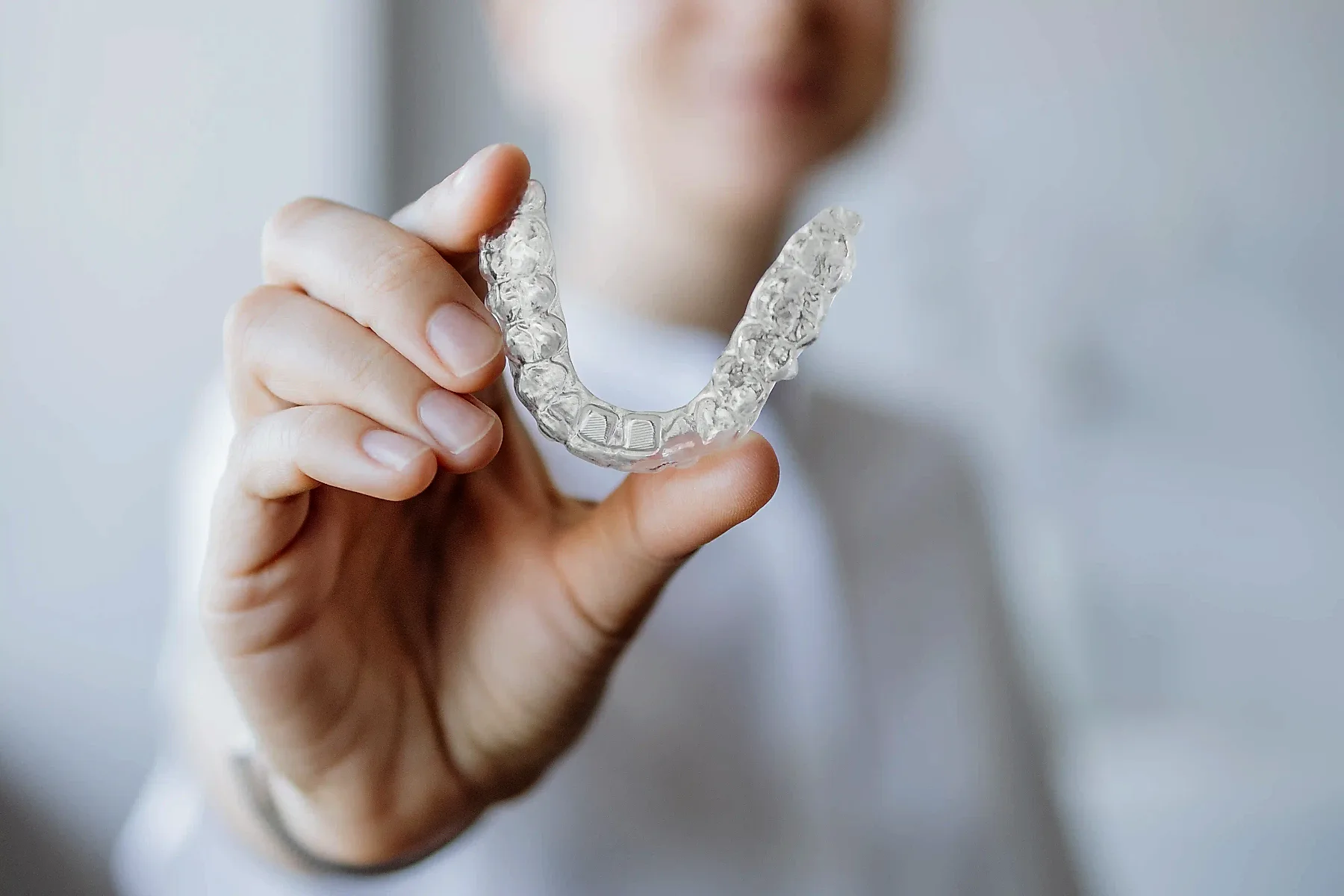 Smiling adult patient holding a clear Invisalign aligner at Harmony Orthodontics