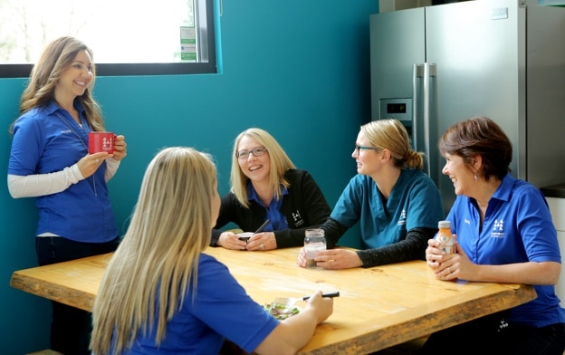 Women in blue shirts talking and laughing at table.
