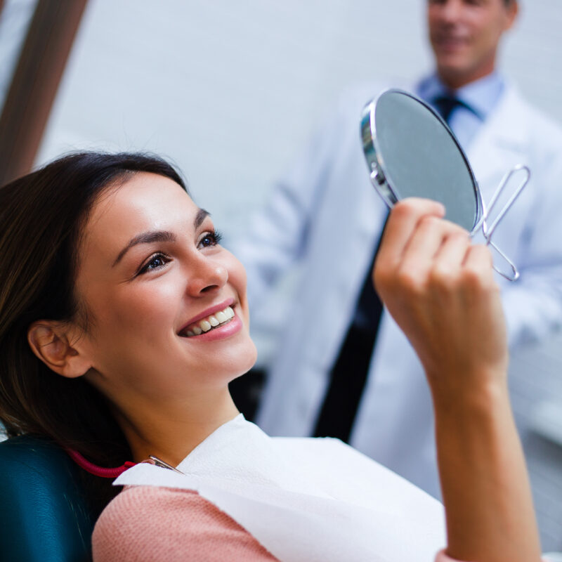 happy women smiling with white teeth into a mirror at her ortho appointment
