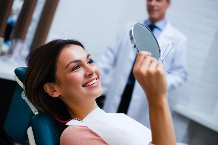 happy women smiling with white teeth into a mirror at her ortho appointment